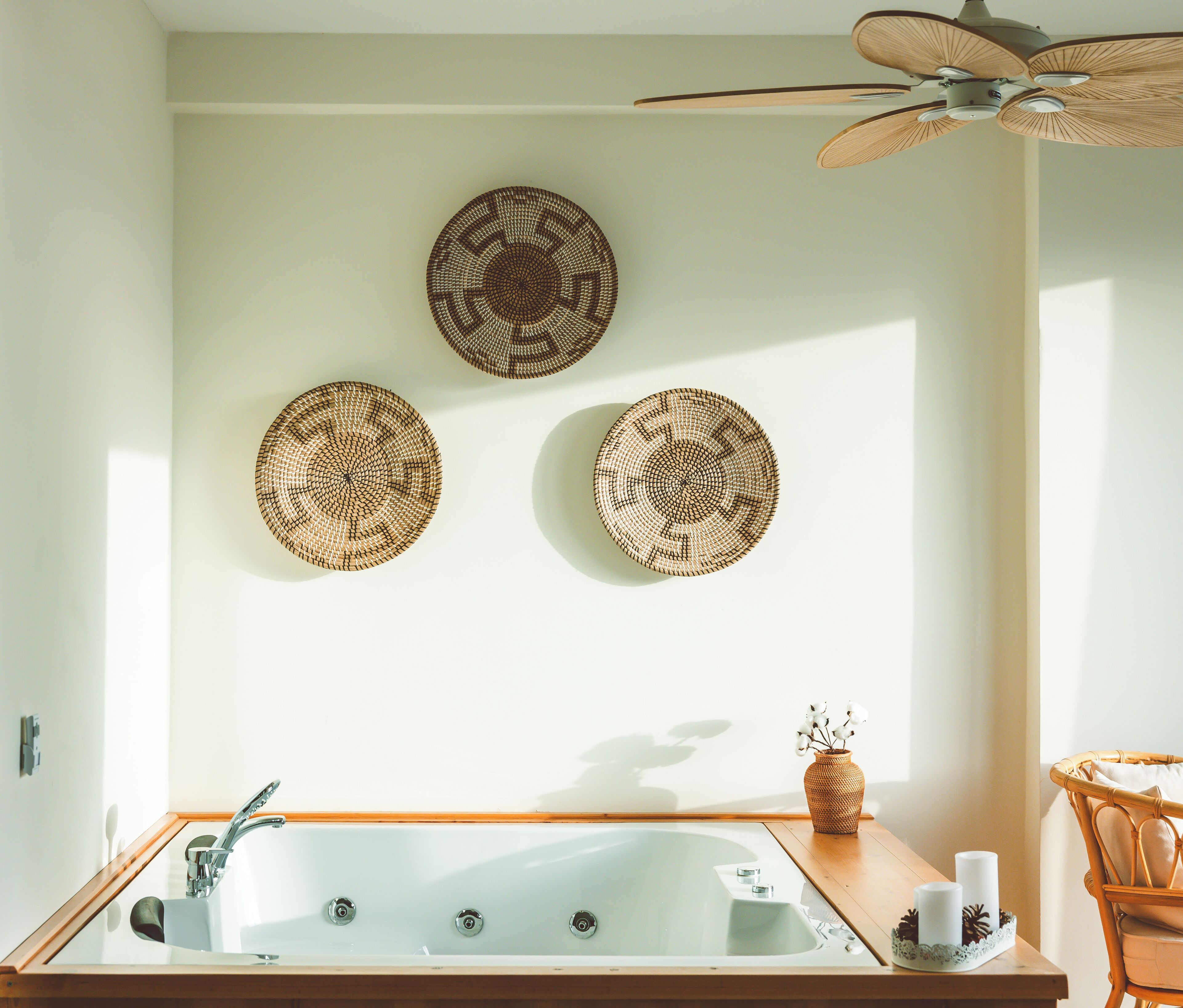 A bathroom with a bathtub, a ceiling fan, and three woven wall decorations.