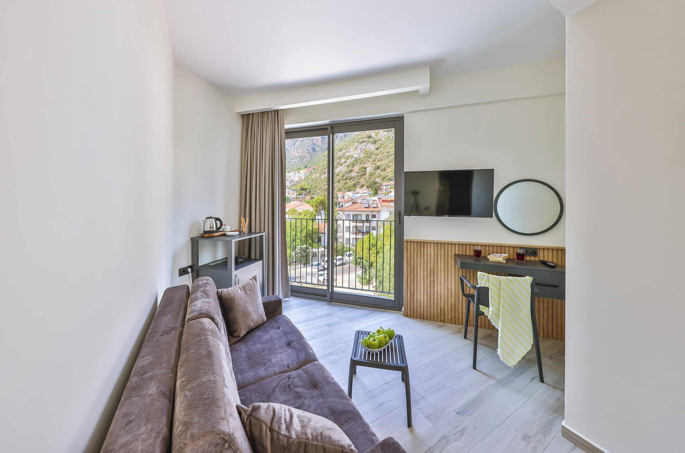 A modern living room with a sofa, a small table with apples, a TV, and a view of the city through large windows.