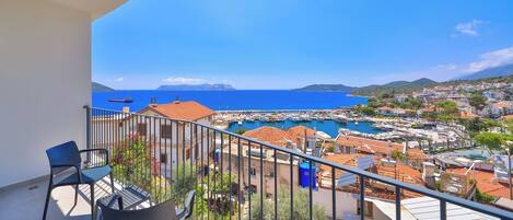 A balcony with two chairs, a view of a marina with boats, and a coastal town in the background.