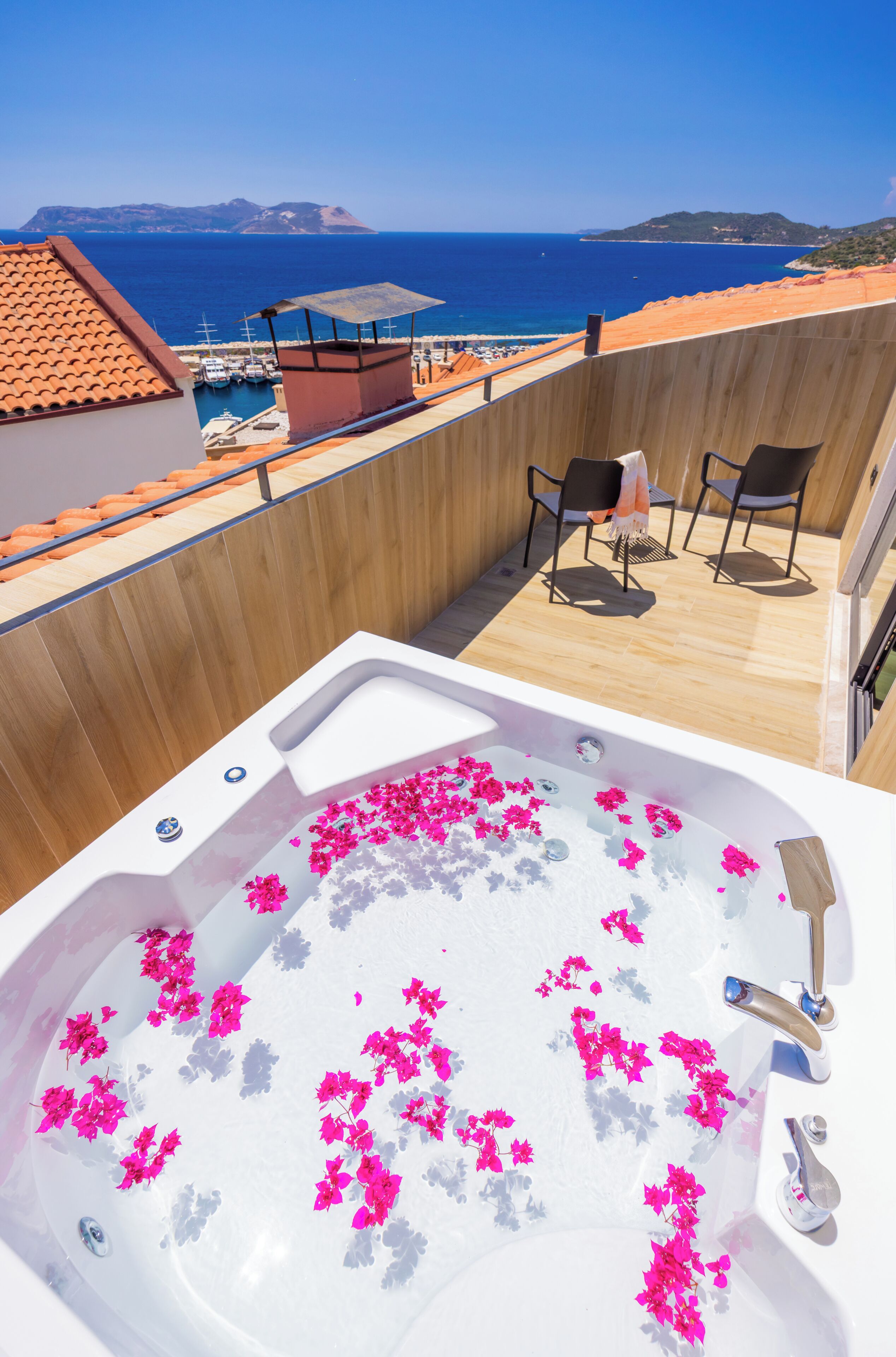 En tagterrasse med jacuzzi, stole og havudsigt.