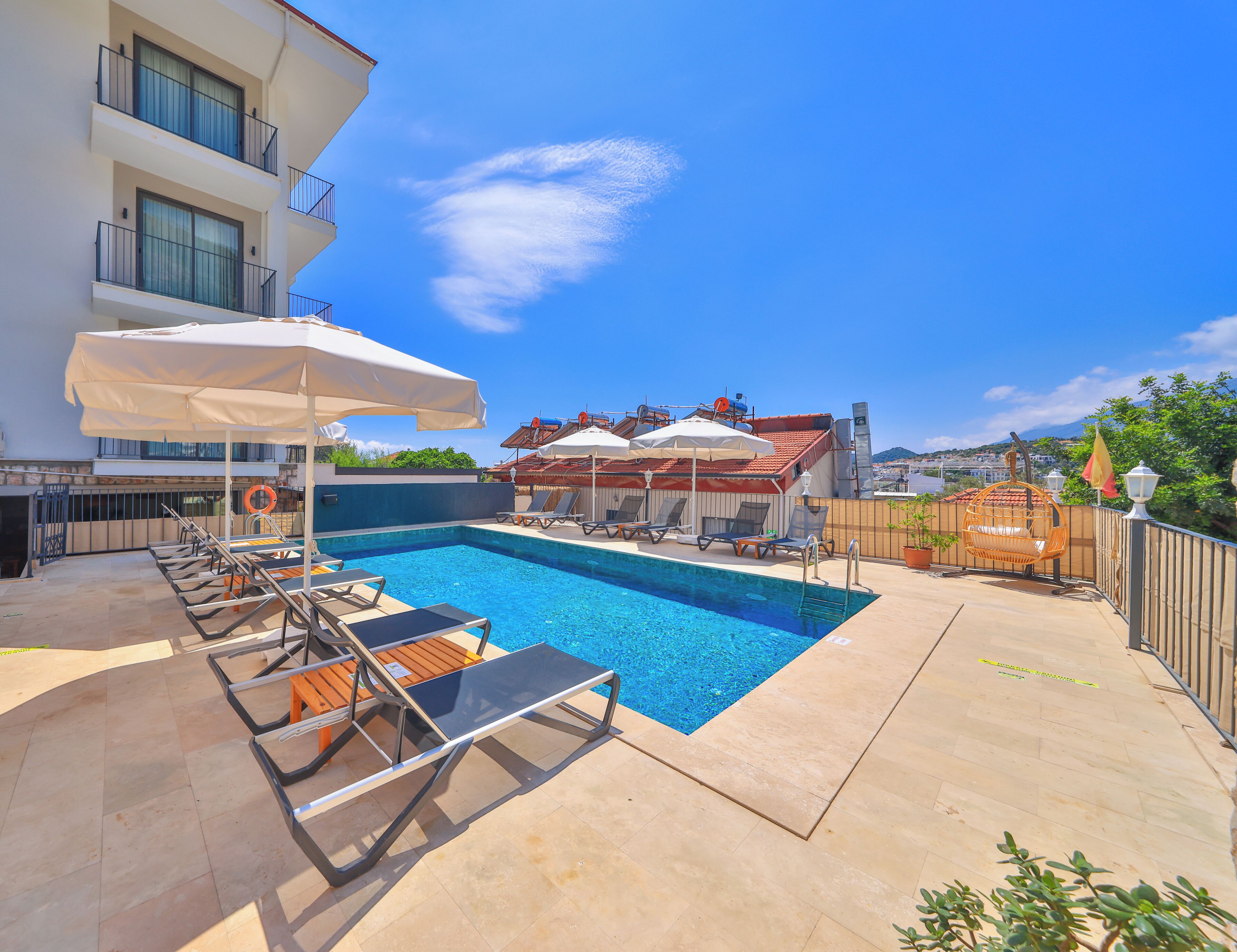 A swimming pool with lounge chairs and umbrellas, a building with balconies, and a clear blue sky.