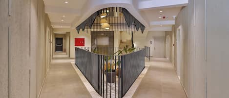 A modern hotel lobby with a curved staircase, a red emergency exit sign, and a potted plant.