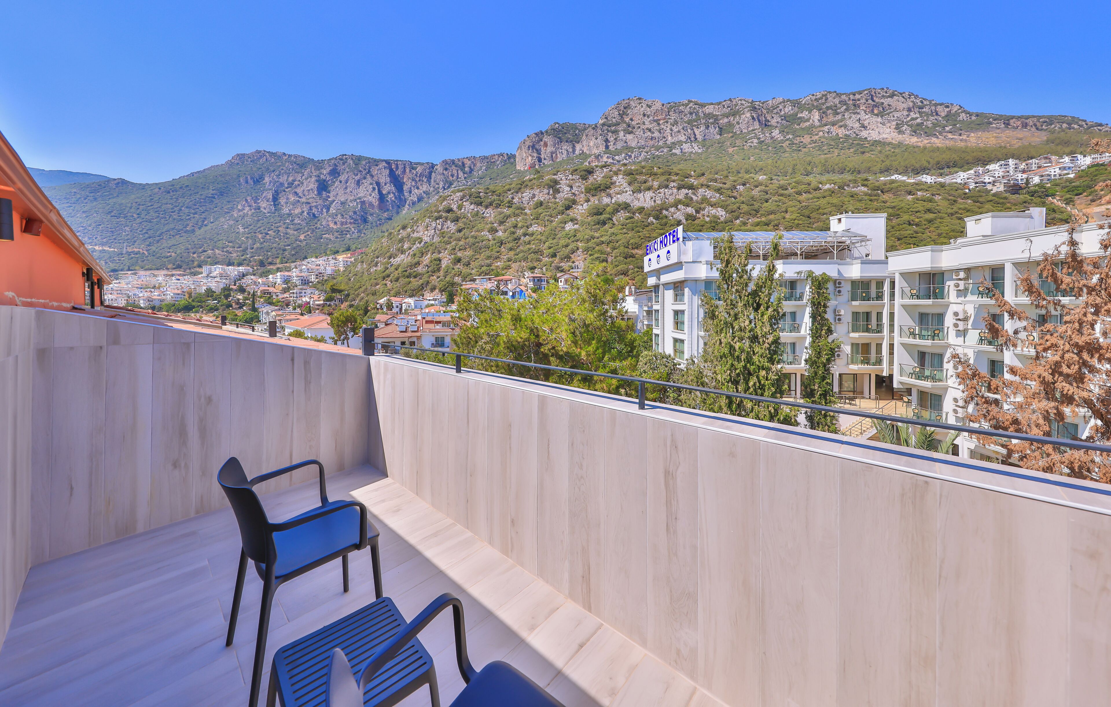 A balcony with a view of a mountainous landscape, a hotel building, and a clear blue sky.