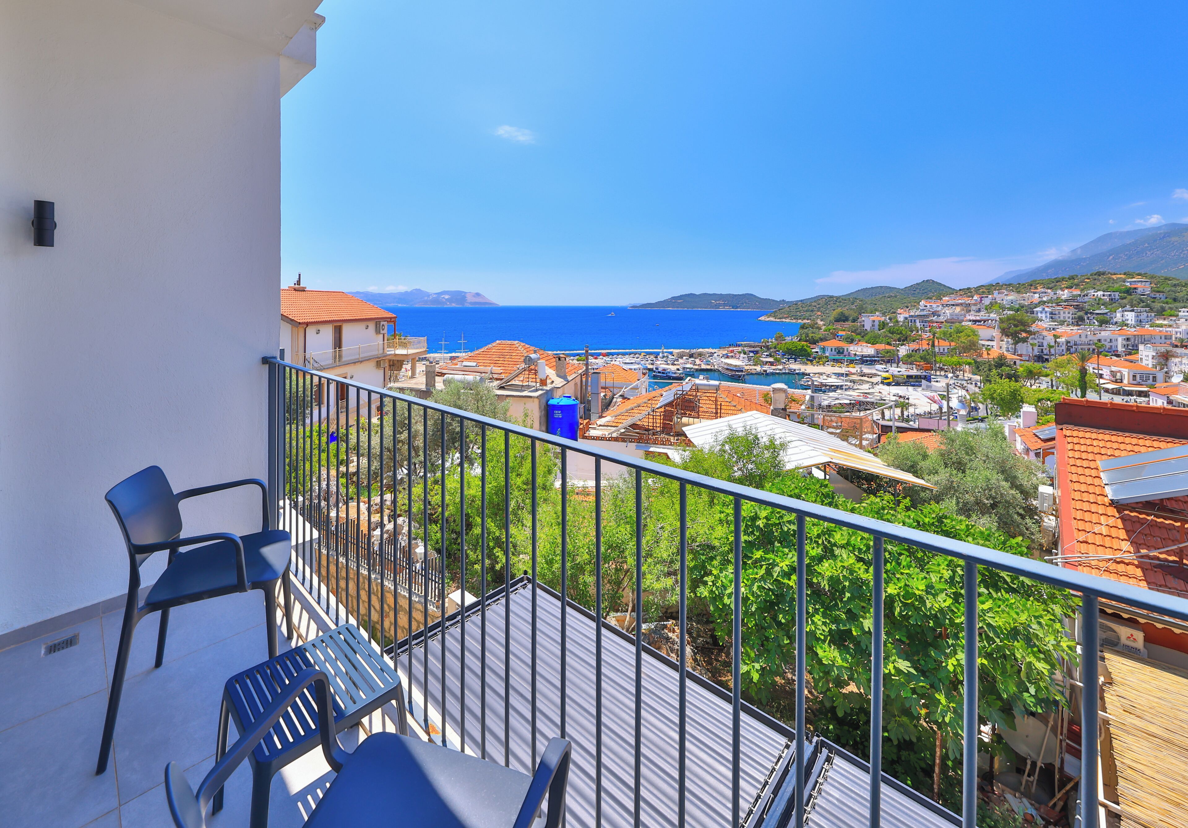 A balcony with chairs, a view of a coastal town, and a clear blue sky.