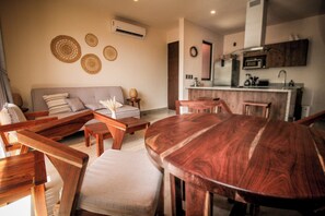 Una sala moderna con una mesa de comedor de madera, un sofá y una zona de cocina con microondas y fregadero.