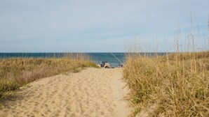 Een zandpad dat naar een strand leidt, met een voertuig en mensen in de verte.