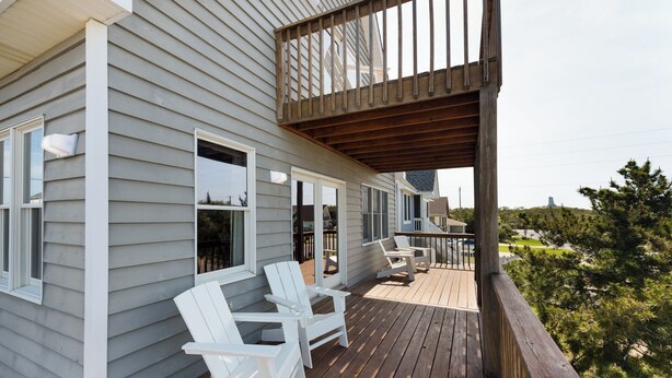 Een houten terras met witte stoelen en een balkon met uitzicht op een woonwijk.
