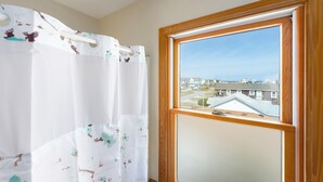 Een badkamer met douchegordijn met een natuurprint, een raam met uitzicht op huizen, en een houten lijst.