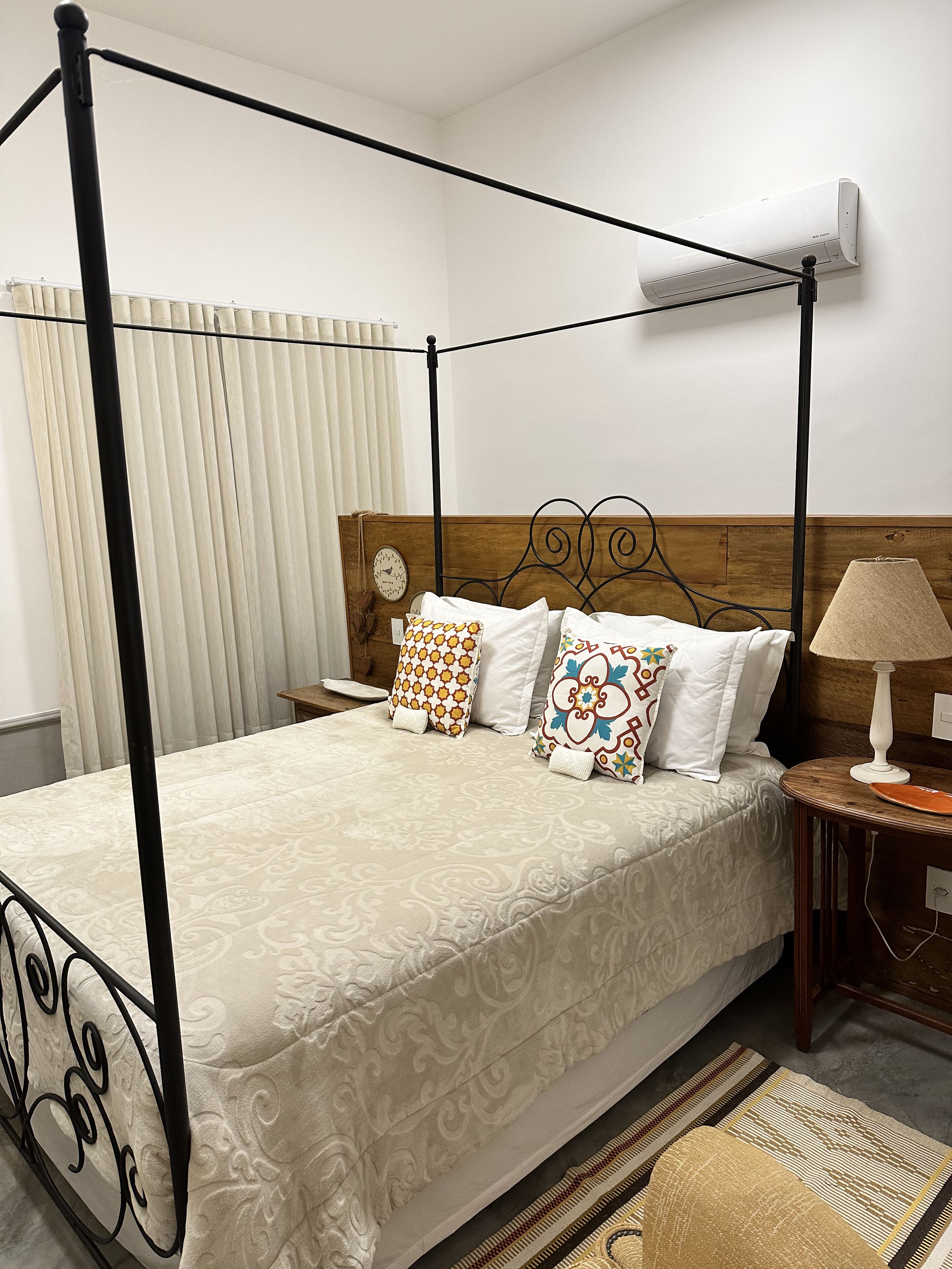 A four-poster bed with a wooden headboard, a bedside table with a lamp, and a wall-mounted air conditioner.