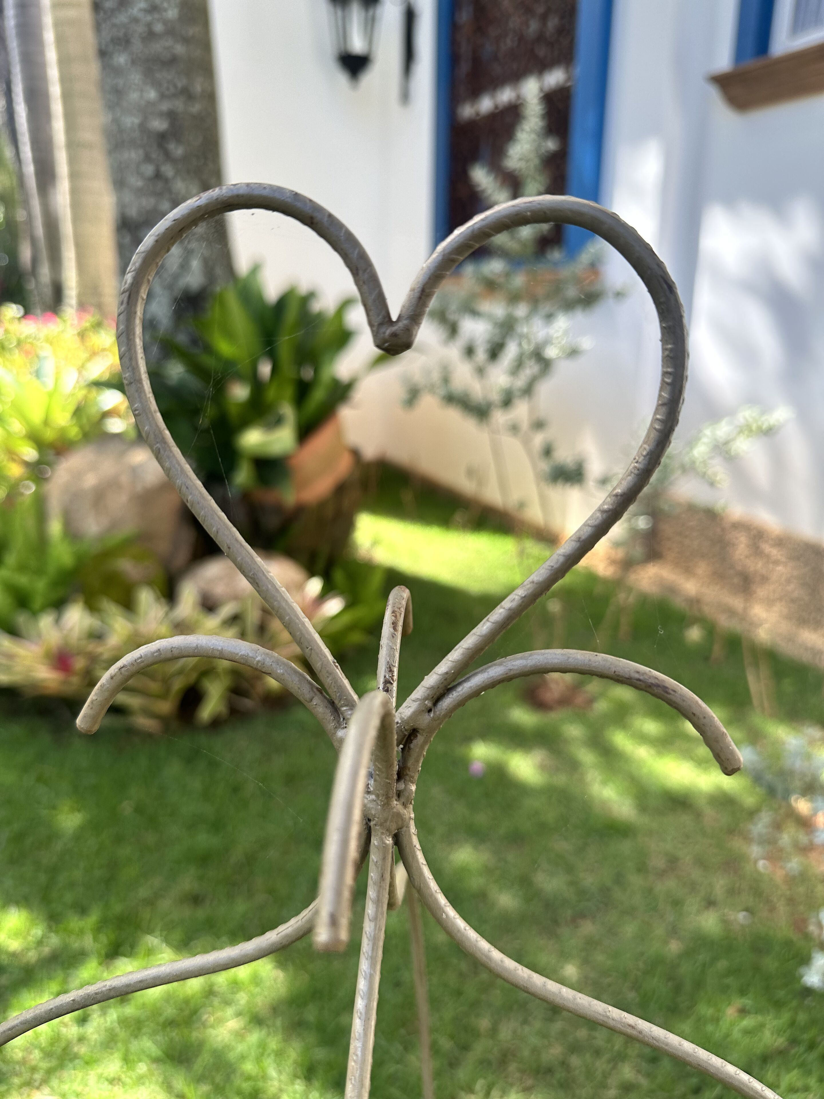 Una escultura metálica con forma de corazón en un jardín, con una casa al fondo.