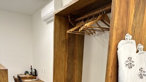 Een houten garderobe met kledingroede en een bankje, een houten tafel met een waterkoker, en een witte badjas met borduurwerk.