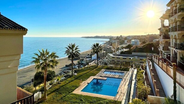 Ein Pool mit Blick auf Strand und Meer, umgeben von Gebäuden und Palmen.