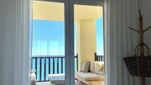 Ein Zimmer mit Bett, Blick auf einen Balkon mit Tisch und Stühlen sowie einem Korbwäschekorb an der Wand.