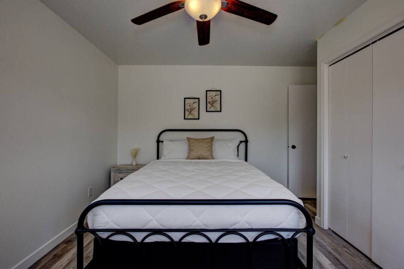 Een slaapkamer met een bed, nachtkastje, plafondventilator en kledingkast.