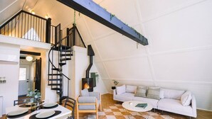 A loft-style living space with a staircase, a fireplace, a sofa, and a dining area. - Secluded A-Frame Hocking Hills: Hot Tub, Fire Pit (South Bloomingville)