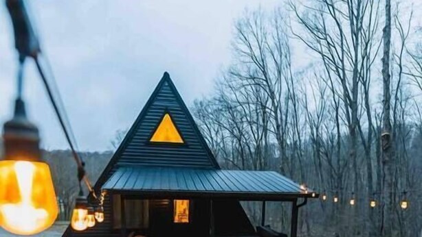 A cabin with a triangular roof, a porch with seating, and a fire pit. - Secluded A-Frame Hocking Hills: Hot Tub, Fire Pit (South Bloomingville)