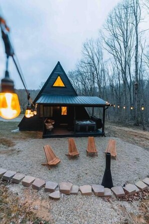 Une cabane avec un toit triangulaire, une véranda avec des sièges et un foyer.