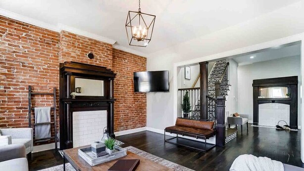 A living room with a brick wall, a fireplace, a television, and a staircase. - Spacious 4BR/3.5BA Home Near UD, Oregon &DT Dayton (Dayton)