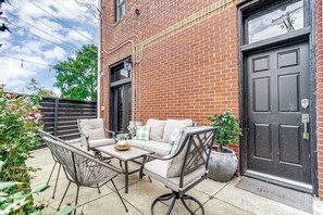 An outdoor patio with a brick wall, a black door, and a seating area with a table and chairs.