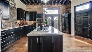 A modern kitchen with dark cabinetry, a central island, and a brick wall. - Dayton Loft close to DT, Oregon, UD (Dayton)
