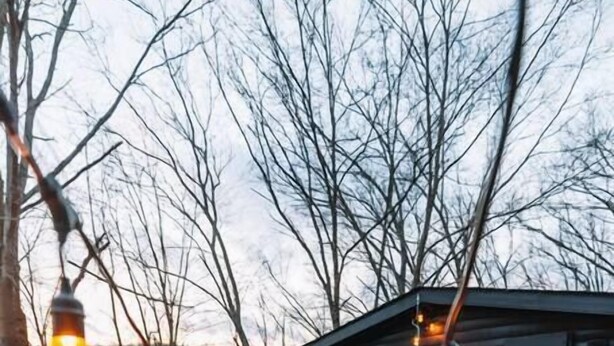 A rustic cabin with a wooden deck, string lights, and a bench.