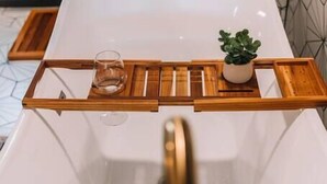 A modern bathroom with a white bathtub, wooden tray, glass, and a potted plant.