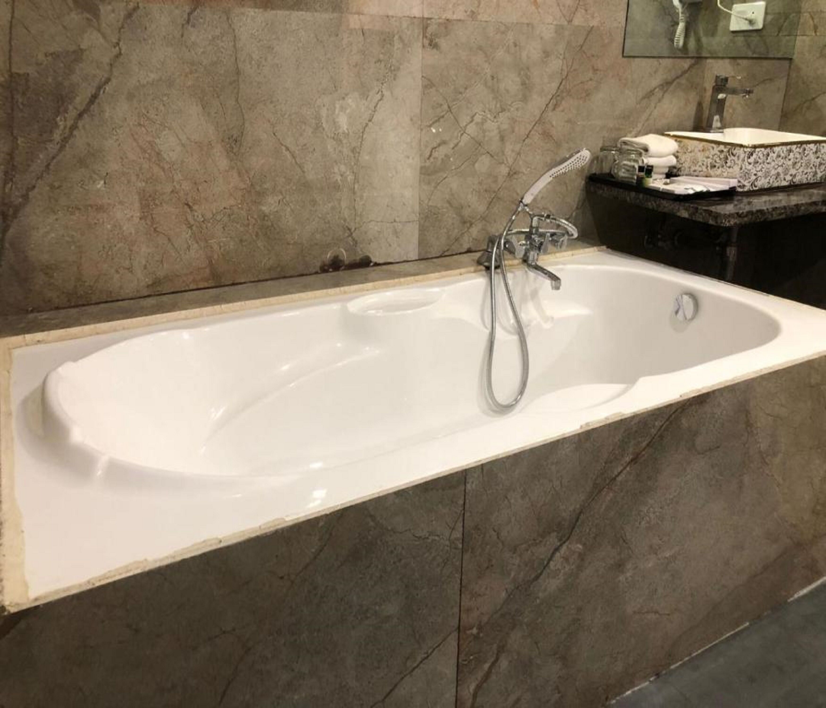 Ein Badezimmer mit einer weißen Badewanne, einer Handbrause und einer Wand aus Marmorfliesen.