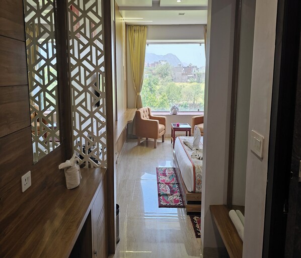Habitación de hotel con escritorio de madera, sofá, una mesita y vistas al exterior.