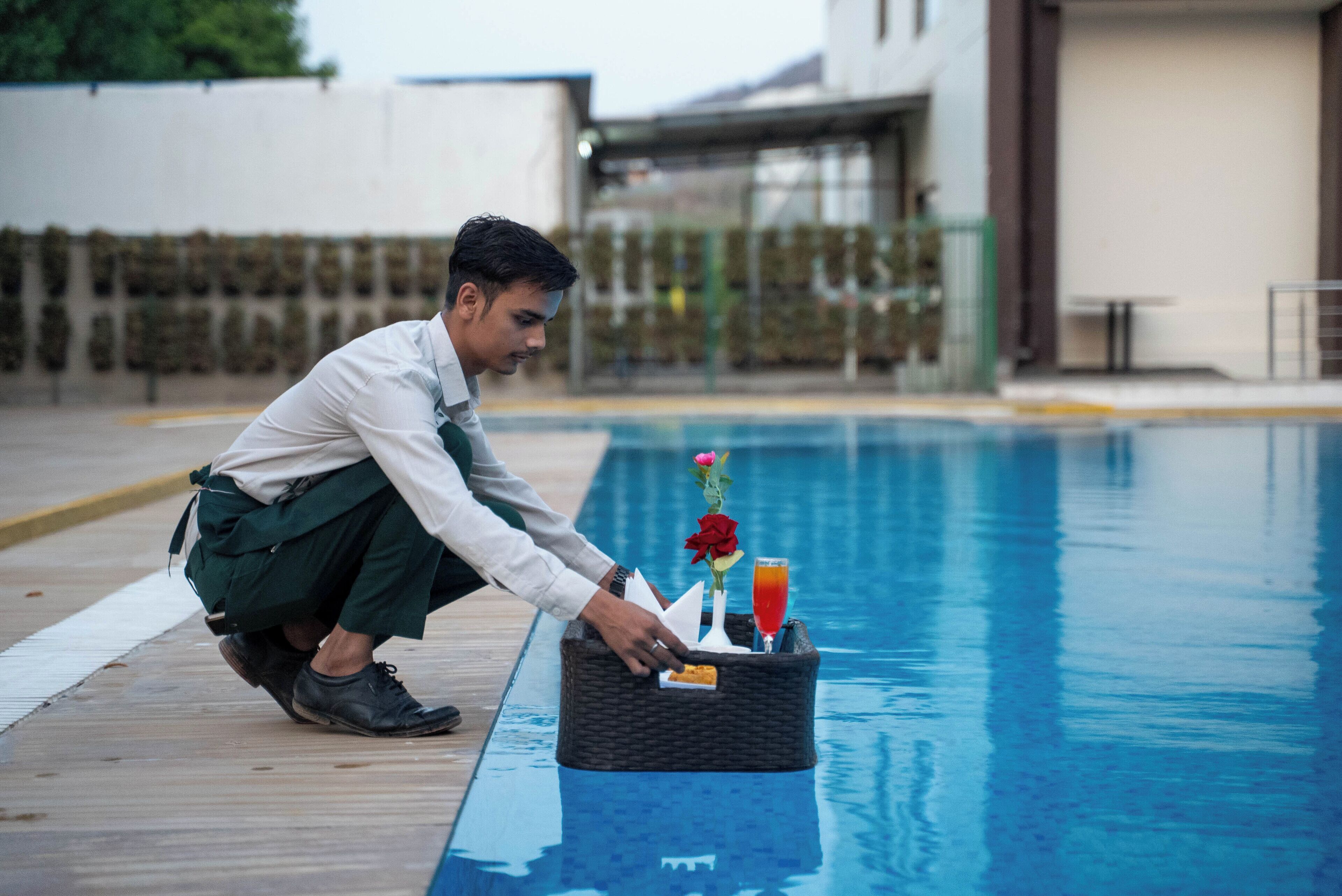 Un hombre junto a una piscina con una cesta que contiene una bebida y una rosa.