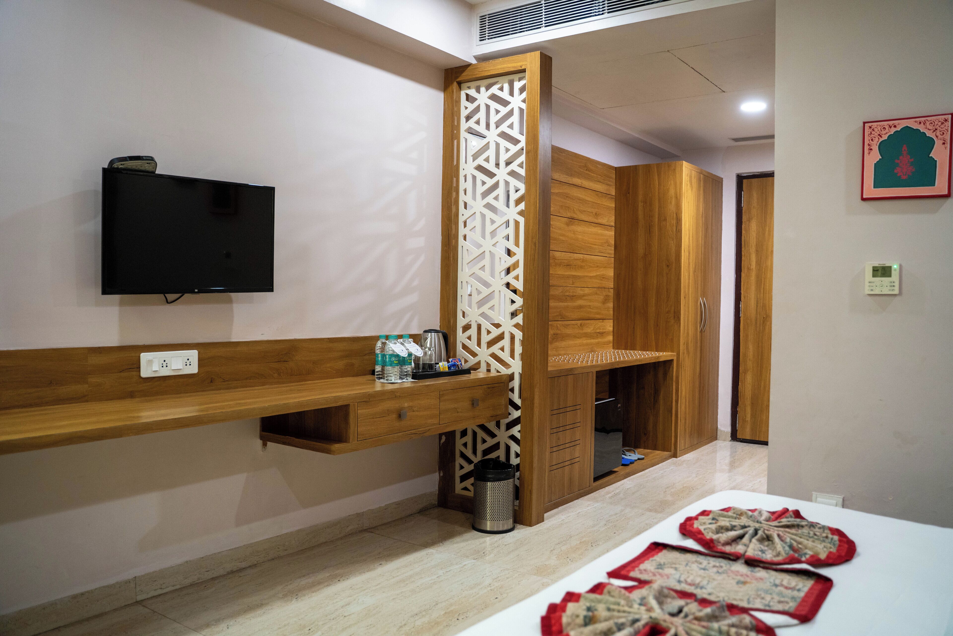 A hotel room with a TV mounted on the wall, a wooden cabinet, a decorative partition, and a table with a placemat.