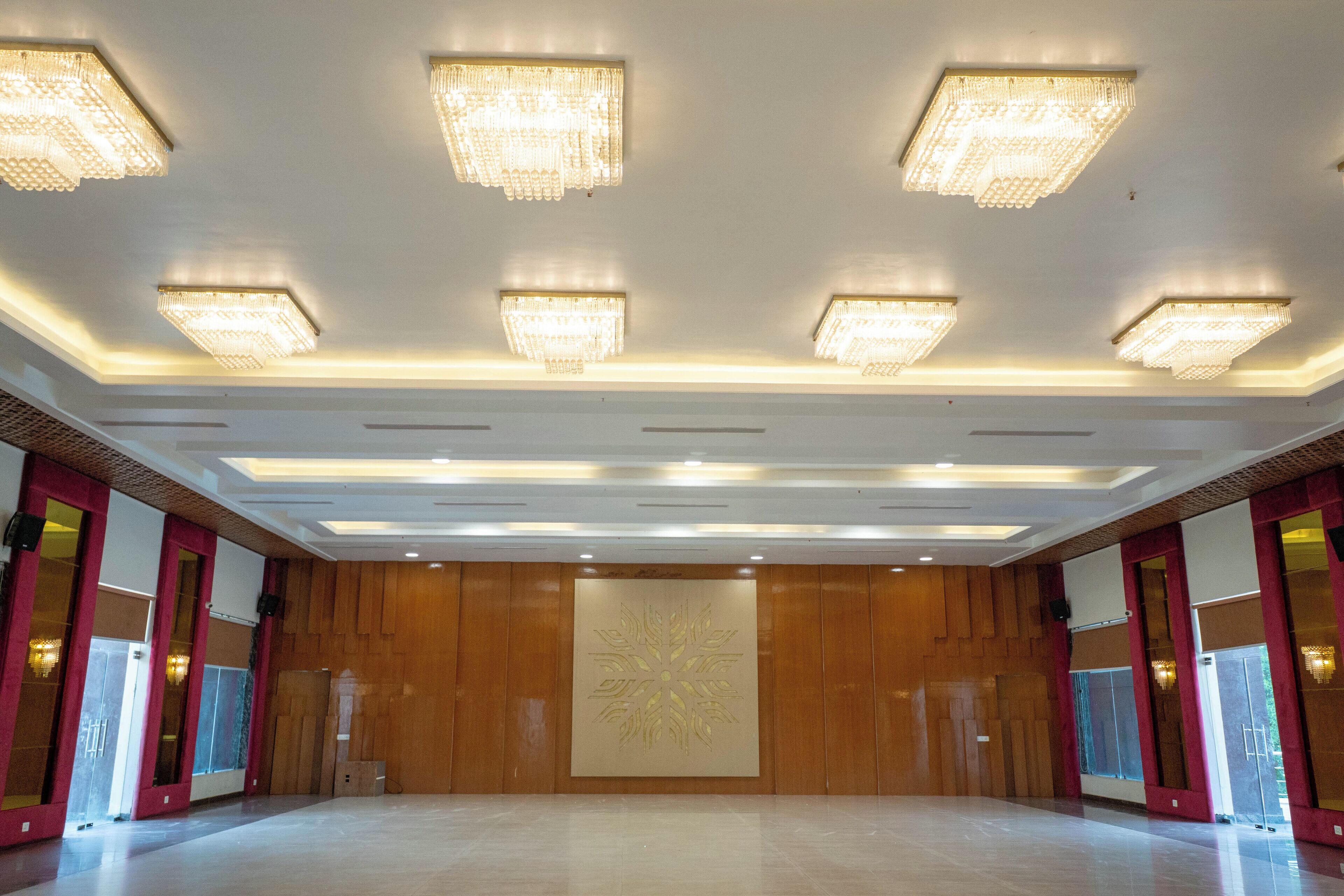 A spacious hall with a polished floor, wooden panel walls, and multiple chandeliers.