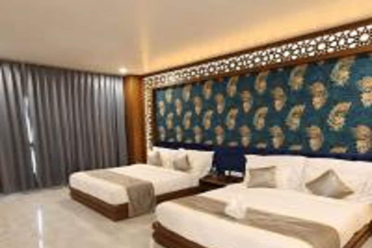 A hotel room with two beds, a patterned headboard, and a large window with curtains.