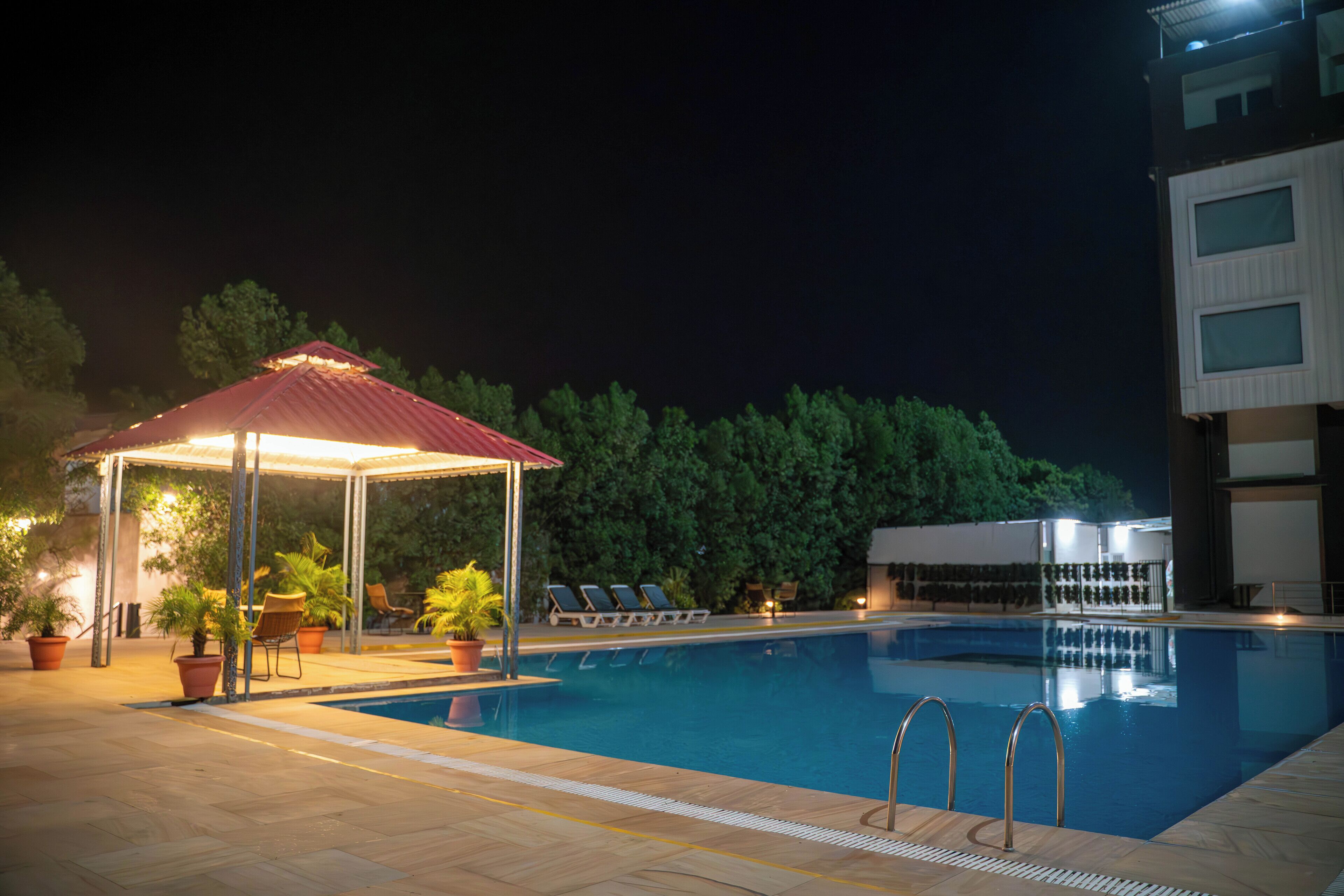 A swimming pool with lounge chairs and a covered seating area at night.