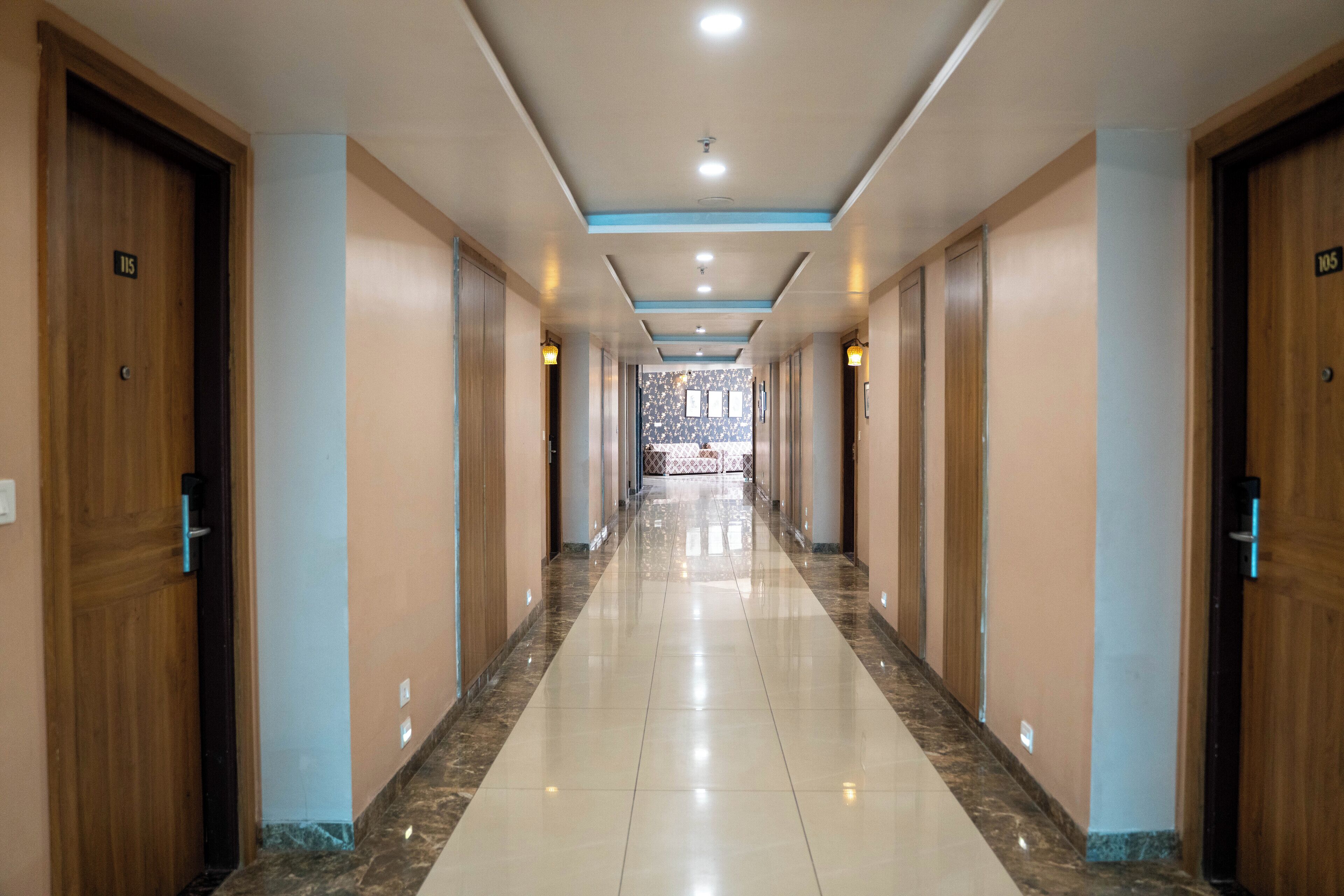 A long, well-lit hallway with wooden doors numbered 115 and 105, leading to a patterned area.