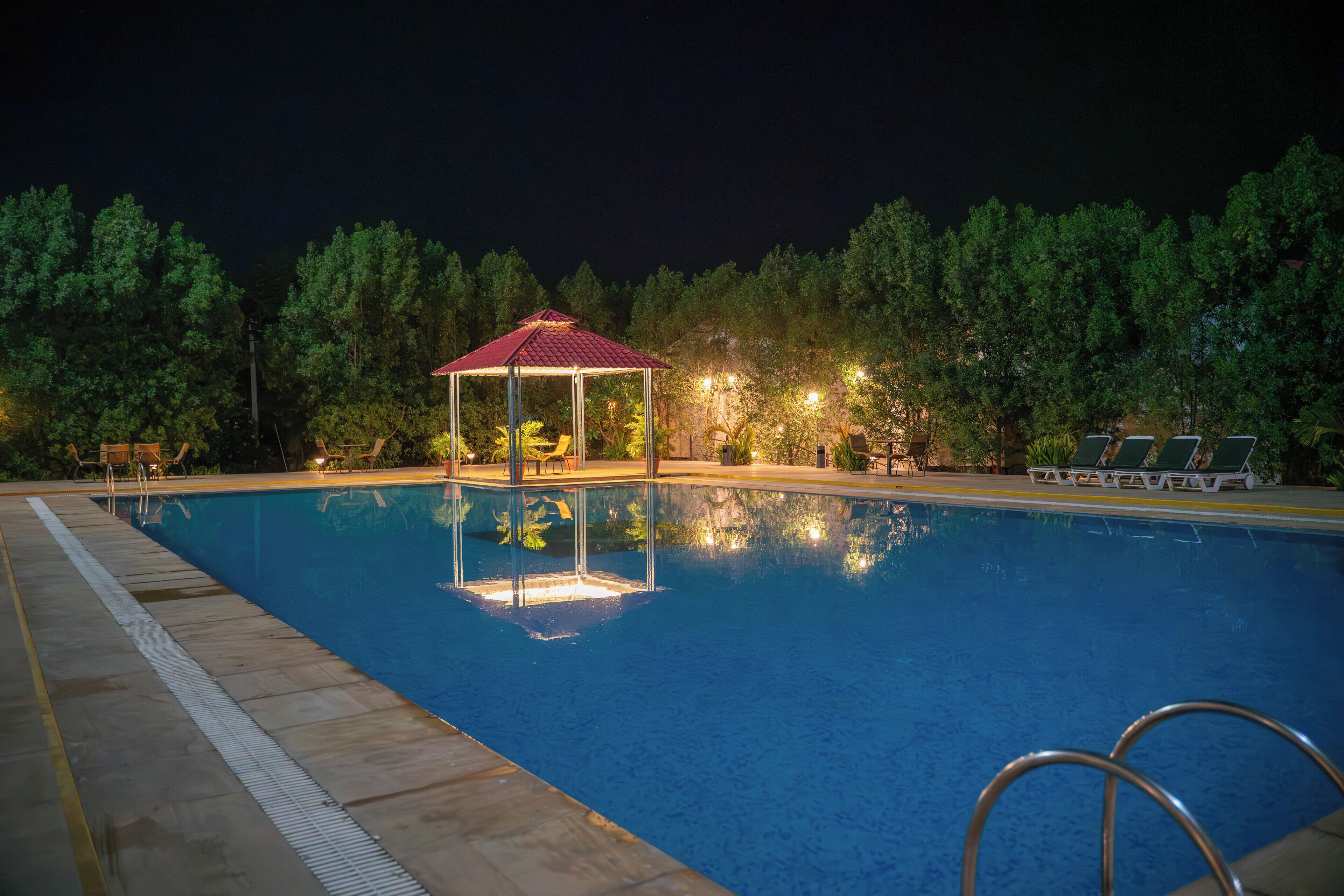 A swimming pool with a gazebo, lounge chairs, and trees in the background.