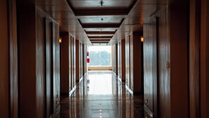 A long, polished hallway with wooden doors and a tiled floor, leading to a bright area with a view of trees. - Bamboo Saa Mulberry Resort Pushkar (Pushkar)