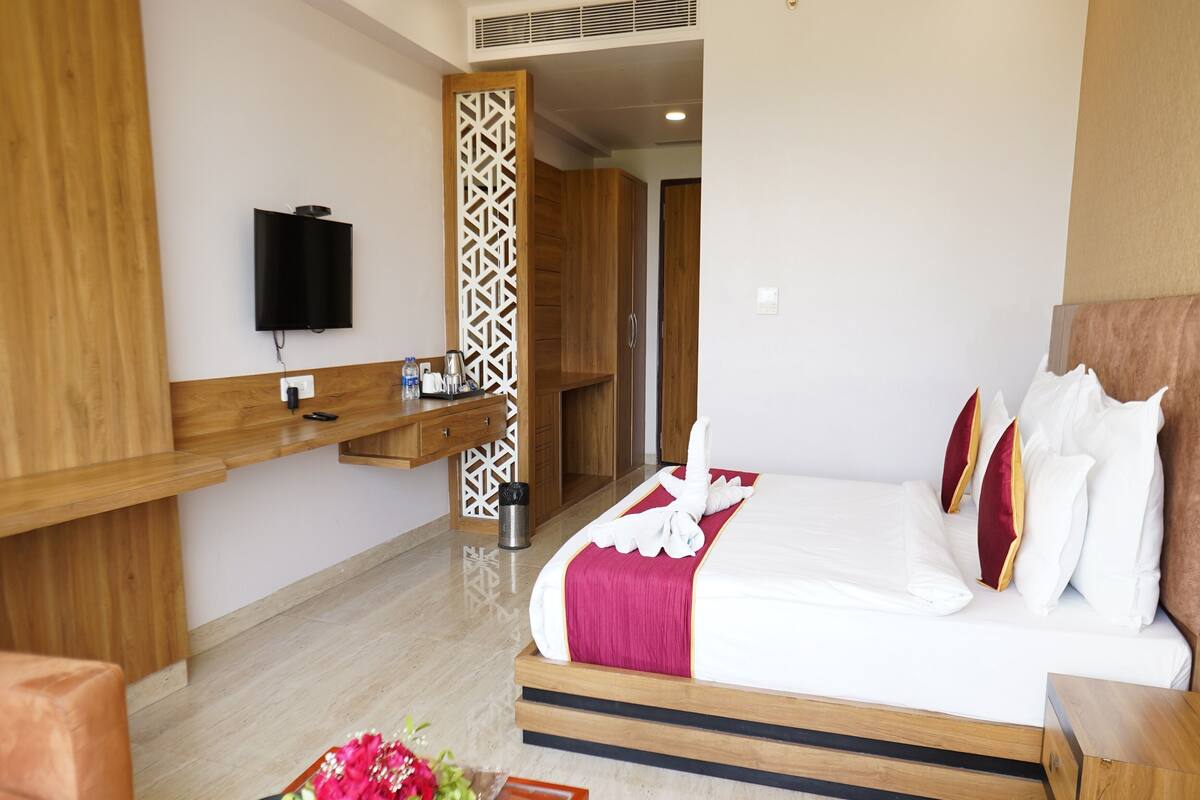 A hotel room with a large bed, a wooden desk, a television, and a decorative partition.