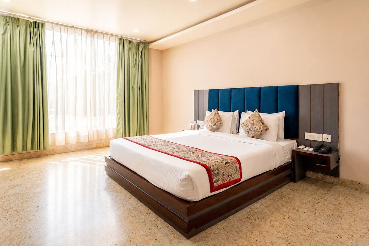 A hotel room with a large bed, a nightstand, a phone, and a power outlet.