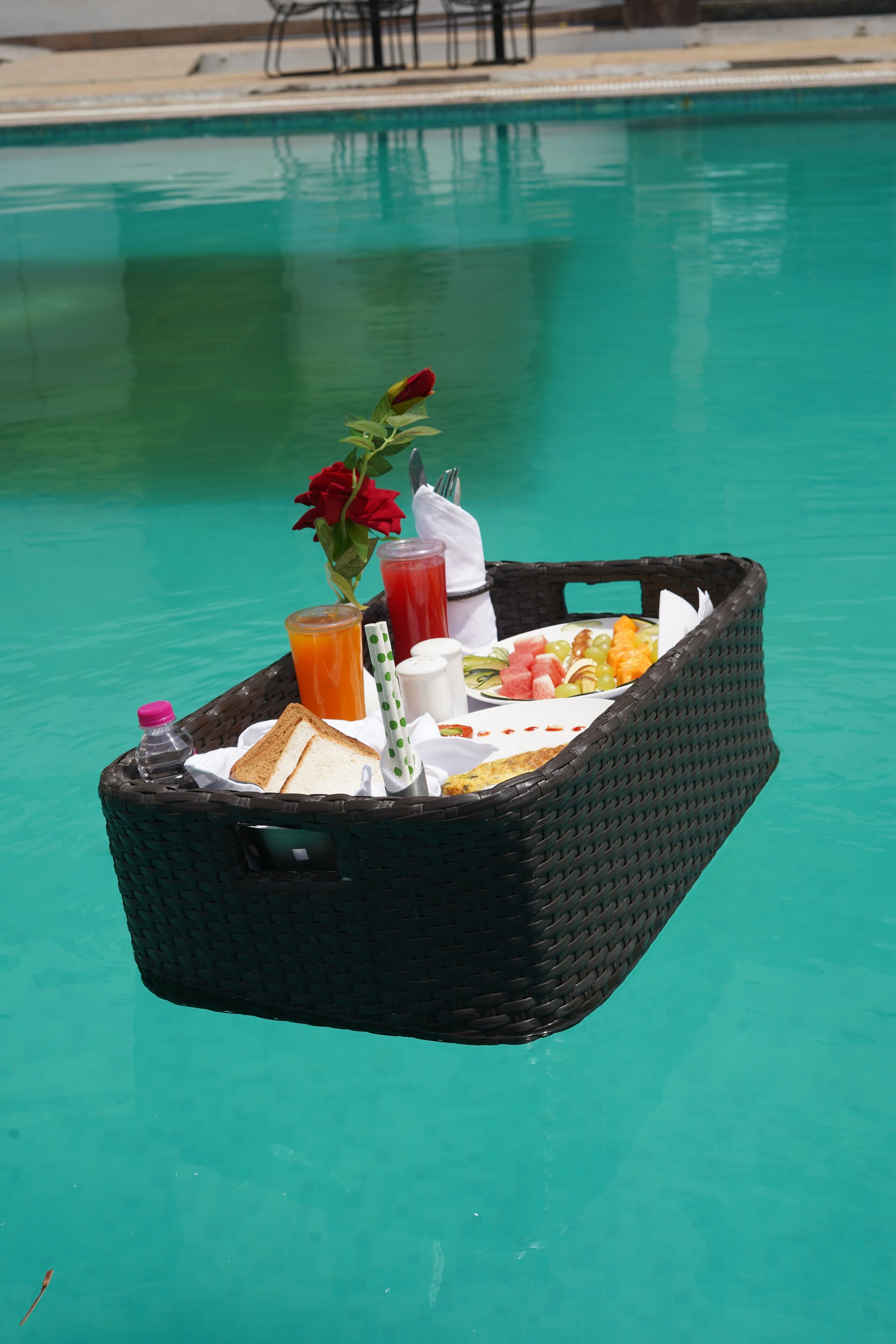 Una cesta de mimbre con alimentos para el desayuno flotando en una piscina.