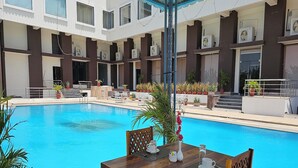 A pool area with a wooden table and chairs, surrounded by potted plants and a building with multiple balconies. - Bamboo Saa Mulberry Resort Pushkar (Pushkar)