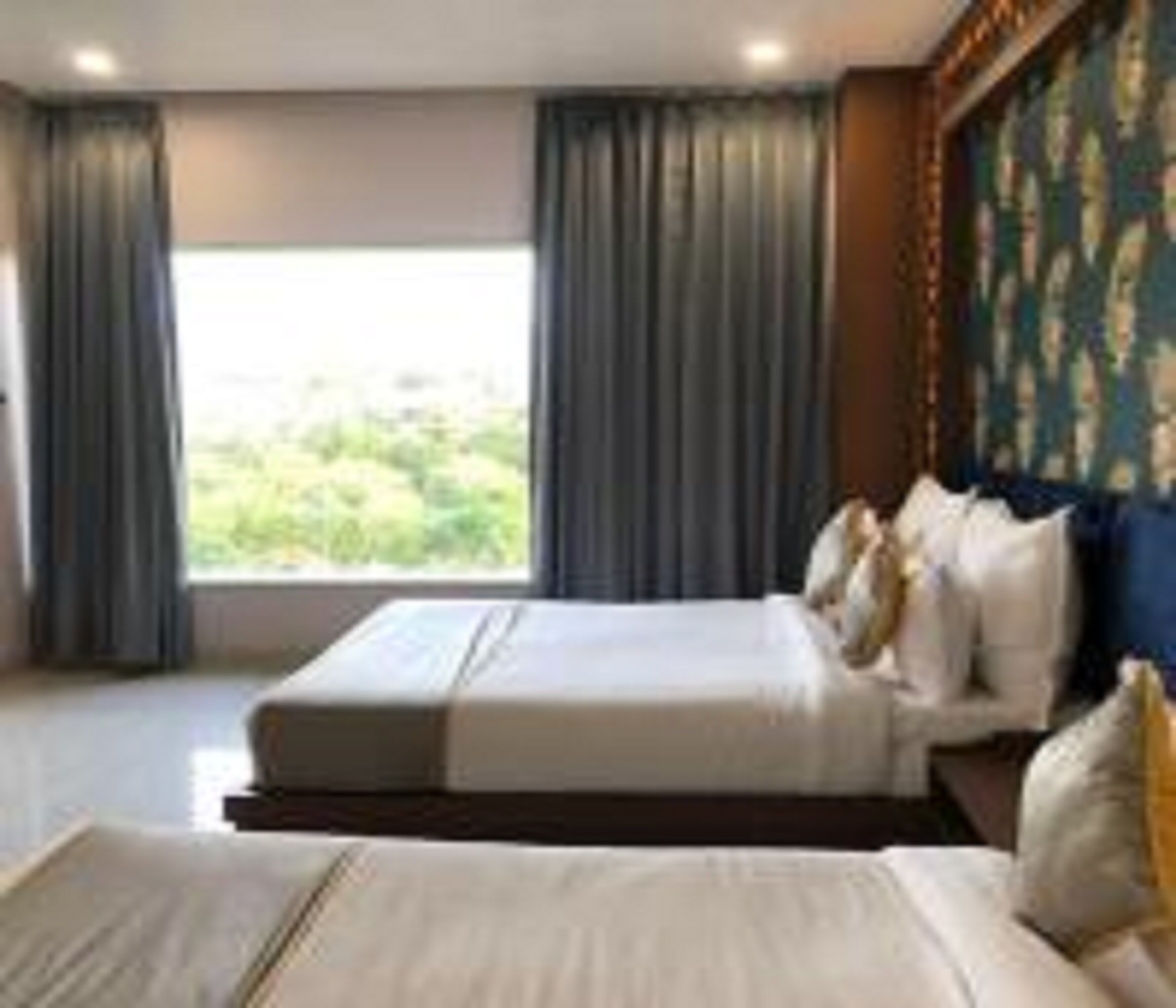 A hotel room with a large bed, a view of greenery outside, and a patterned wall.