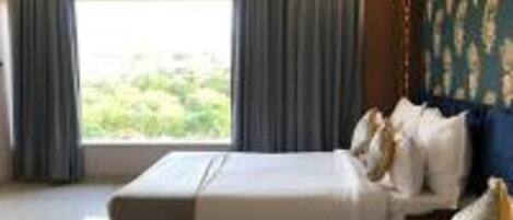A hotel room with a large bed, a view of greenery outside, and a patterned wall.