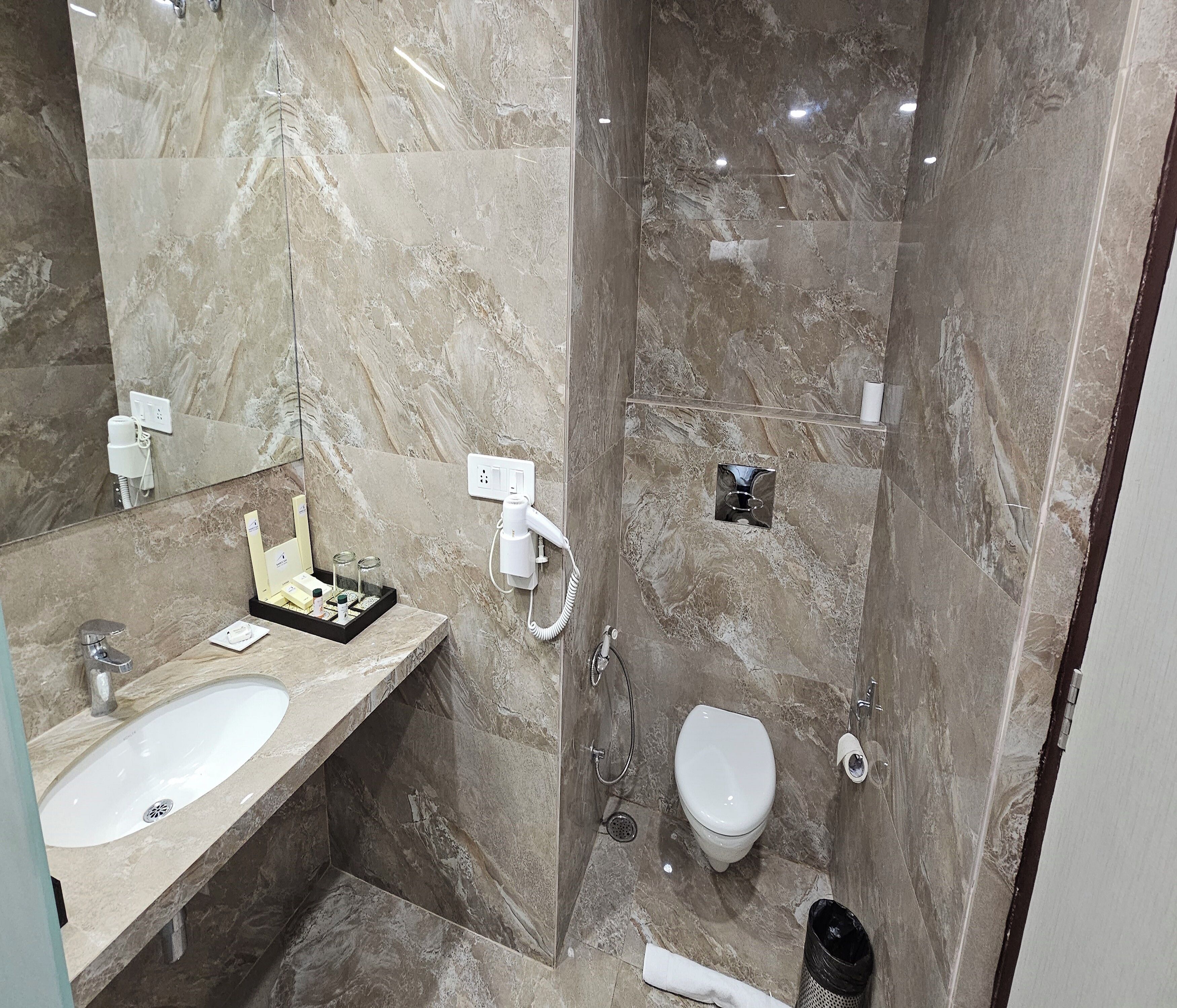 Une salle de bain avec un lavabo en marbre, un miroir, un sèche-cheveux, des toilettes et une douche.