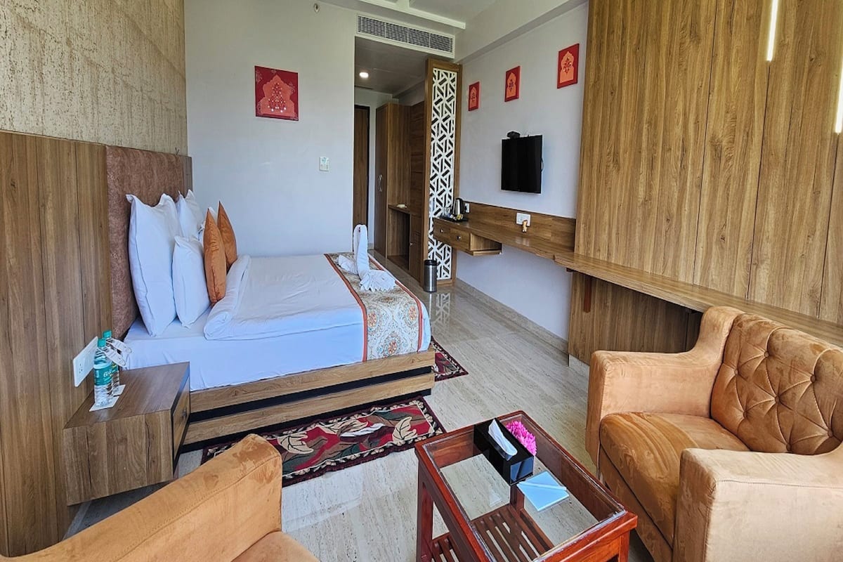 A hotel room with a bed, two chairs, a coffee table, a TV, and a wooden headboard.