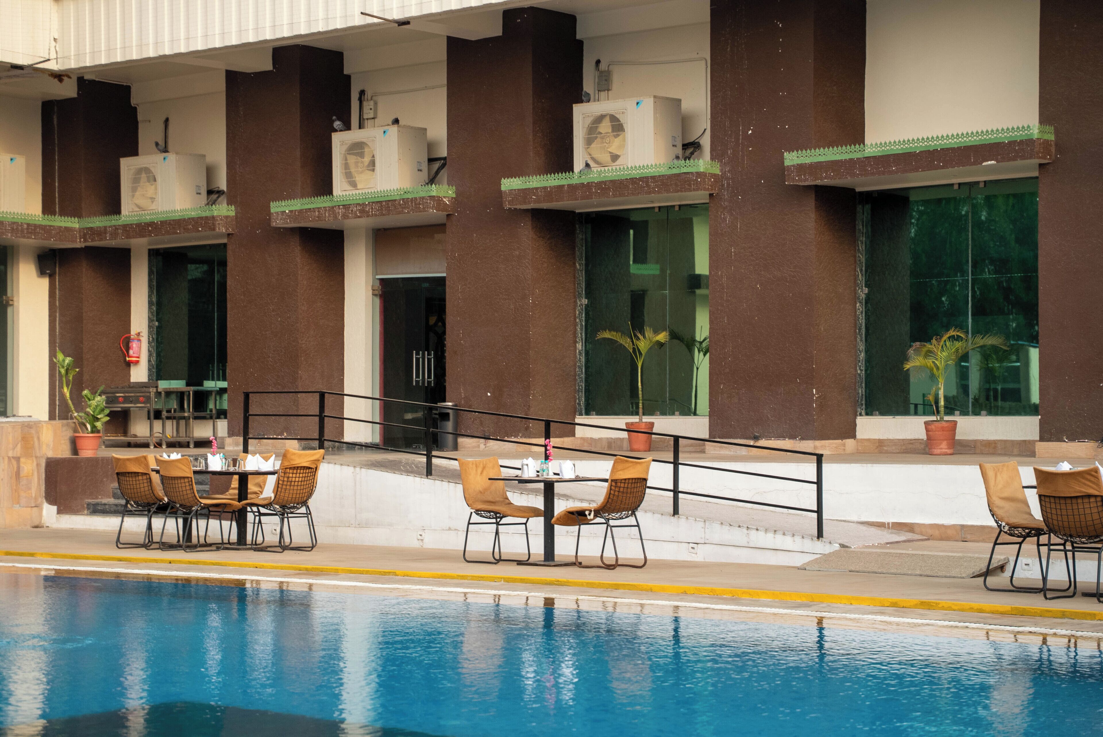 Area piscina con tavolo e sedie, condizionatori nell'edificio e piante in vaso.