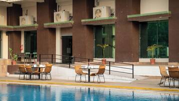Area piscina con tavolo e sedie, condizionatori nell'edificio e piante in vaso.
