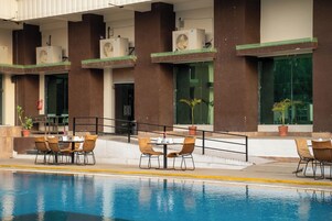 Area piscina con tavolo e sedie, condizionatori nell'edificio e piante in vaso.