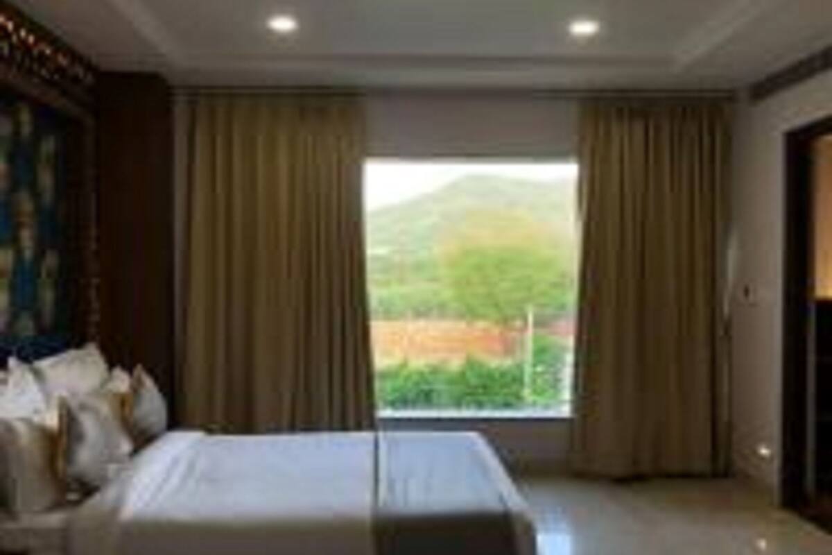 A hotel room with a bed, curtains, and a window with a view of greenery.