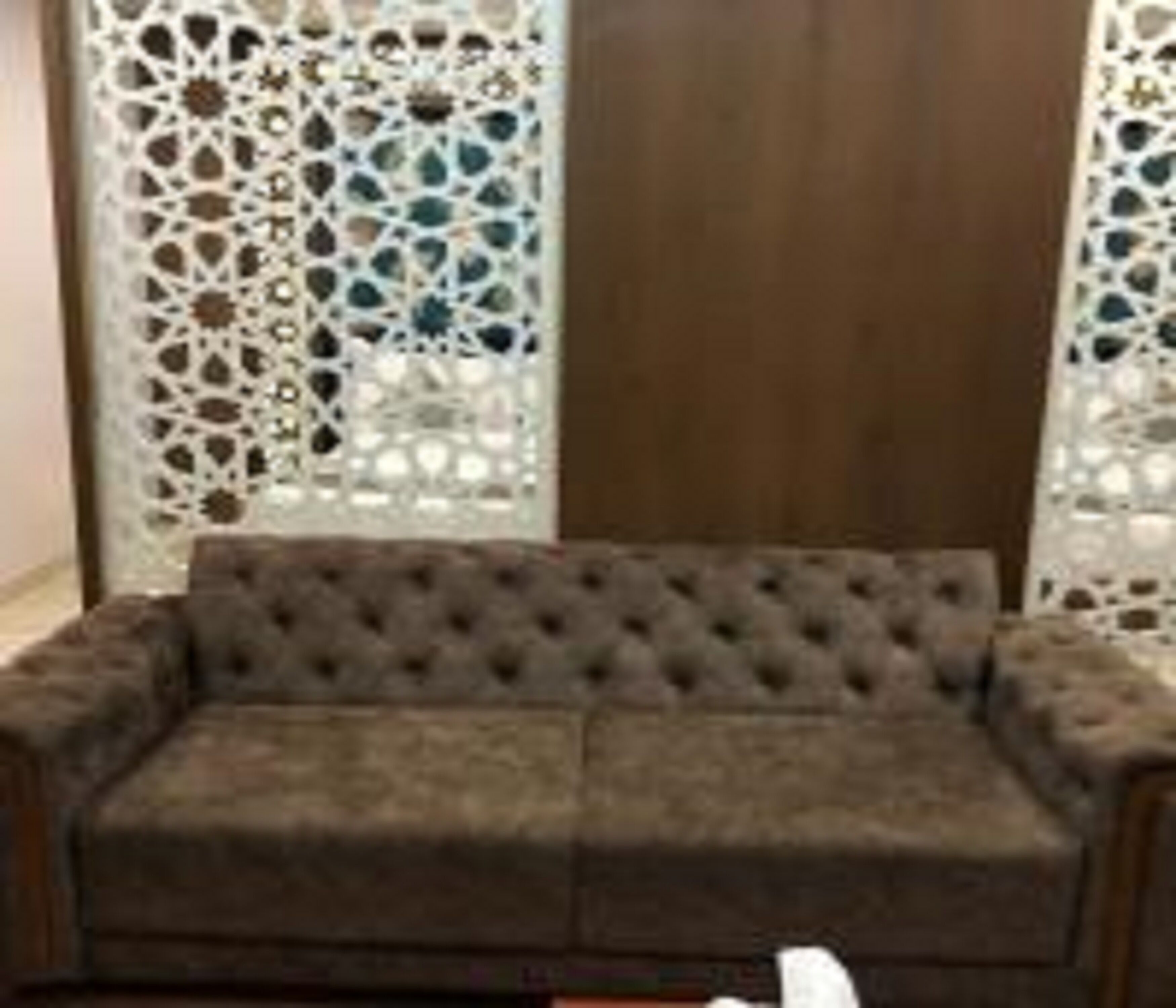 A grey tufted sofa in a room with a wooden door and decorative white lattice panels.