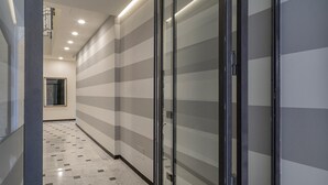 Un couloir aux murs rayés et au sol carrelé, qui mène à une porte dotée d’un panneau de verre.